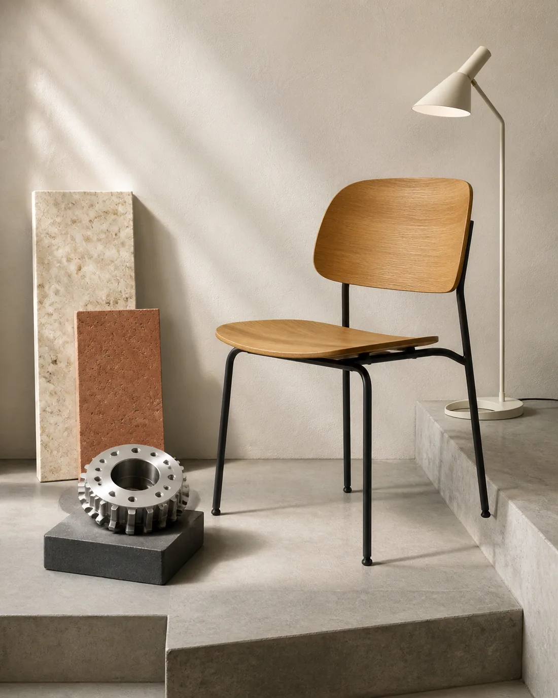 An illustrative arrangement of an oak chair, desk lamp, machined component, and stone material samples